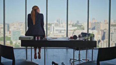 Ofisteki kadın iş yerinde çıplak ayakla oturuyor. Panoramik pencerede güzel şehir manzarası üzerine kafa yoran düşünceli sakin bir yönetici. Yorgun şirket yöneticisi huzurlu anın tadını çıkarıyor..