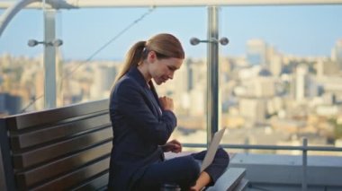 Tarz sahibi serbest çalışan dizüstü bilgisayarın kapağını kapatıyor ve terasta sonuçların keyfini çıkarıyor. Güzel, mutlu bir kadın şehir manzarasında pazarlama projesini uzaktan bitiriyor. Tatmin olmuş genç iş kadını hayal kurmaya ara verdi..