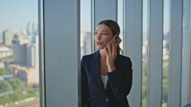 Kadın patron panoramik pencerede hücreden konuşuyor. Şehir manzarasında şirket profesyoneli iş görüşmeleri yapıyor. Güzel bir ofis çalışanı cep telefonuyla iletişim kuruyor. Emlakçı