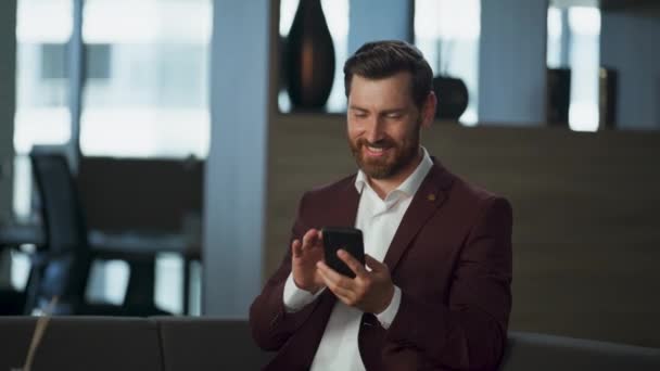 ハッピービジネスマンは 企業の近代的なオフィスでスマートフォンをタイプします 大きいホールの内部の携帯電話の呼出しを終える専門のマネージャーの男 電話を使用して保持している楽しいリアクター 金融業務コンセプト — ストック動画