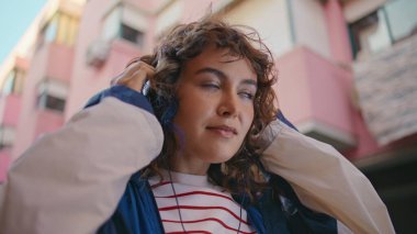 Şehir merkezinde kulaklığını çıkaran bir kız. Kasabanın caddesinde bekleyen çekici kıvırcık kadın. Kulaklıklı, tasasız, mutlu hipster portresi şehir dışında dinleniyor.