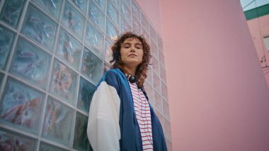 Kıvırcık hippi kentsel alanda poz veriyor. Kameraya yakından bakıyor. Kaygısız bir kadın cam duvara yaslanmış dışarıda sakız çiğniyor. Çekici, rahat, modaya uygun kıyafetli, modern şehirde tek başına duran bir genç..