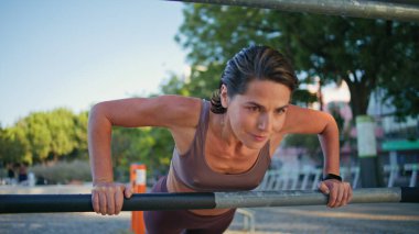 Yaz sokak portresi için kadın pazılarını çalıştırmaya odaklanmış. Açık hava spor salonunda egzersiz yapan aktif bir kadın. Yakın plan. Yatay çubuk kullanarak tahta görünümlü kamerada fitness eğitmeni