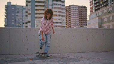 Akşam sokağında kaykay yapan şık bir kadın. Kıvırcık kız kaykaycı şehir bölgesinde uzun kaykayla geziyor. Hafta sonları açık havada havalı hipster eğitimi. Etkin yaşam biçimi.