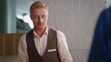 Resepsiyonda dost canlısı konuklar konuşuyor. Üniformalı gülümseyen adam lobideki otel müşterilerine pasaport veriyor. Profesyonel servis elemanı. Müşteri yöneticisi çiftlerle iletişim kuruyor.