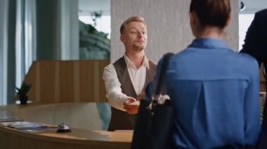Resepsiyonist, otel müşterilerine yakın çekimde yardım ediyor. Turist çift ödemeyi tezgahta yapıyor. Arkadaş canlısı profesyonel bir adam terminale ziyaretçilere yardım ediyor. İşlem sırasında müşteri hizmetleri kavramını kontrol et.