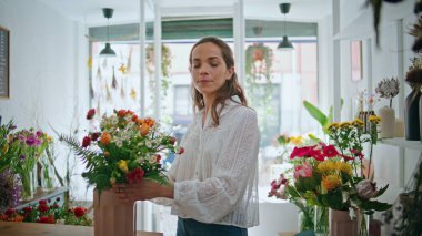 Yakın plan mutlu çiçek perakendecisi fabrika atölyesindeki kameraya bak. Neşeli kadın dekoratör çiçekçide çiçek buketinin tadını çıkarıyor. Yerel işletme sahibi gülümseyerek butikte baharın tadını çıkarıyor. Çalışma konsepti