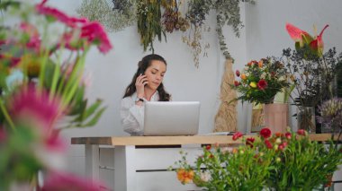 Çiçekçi dükkanında çalışan cep telefonu müşterisi. Çiçekçi dükkanında dizüstü bilgisayarı olan meşgul bir girişimci. İş kadını akıllı telefon dijital cihazını çalıştırıyor. Modern konsept.