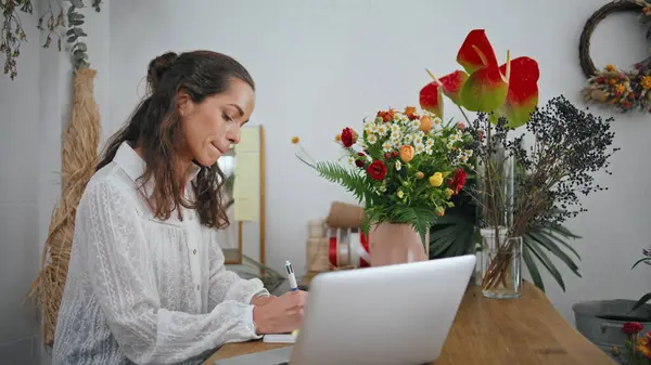 Focused entrepreneur work flowers shop table. Thoughtful woman florist write task goals using notebook paper in store close up. Pensive floral worker create make business ideas. Job workplace concept.