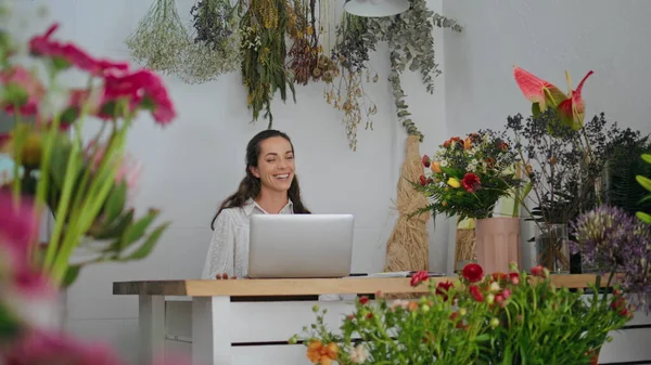 Welcoming woman florist work in flower store. Happy business owner smiling in plant shop close up. Young entrepreneur enjoy working career in floral botany. Pretty girl browse laptop. Job concept.