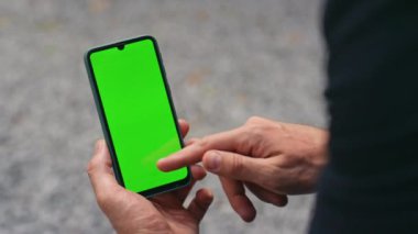Yakın plan parmak yeşil akıllı telefon ekranına dokunuyor. Sokakta el ele tutuşan cep telefonu cihazı. Tanınmayan işadamı kroma tuşlu cep telefonu sohbetini çevrimiçi kontrol ediyor. Uygulama kullanıcı kavramı