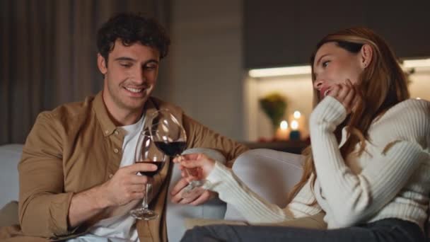Młodzi Małżonkowie Pijący Wino Razem Świętujący Rocznicę Domowej Kanapie Uśmiechnięta — Wideo stockowe