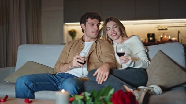 已婚夫妇拿着酒杯躺在沙发上休息 无忧无虑的夫妻在家里享受浪漫的夜晚约会 爱看电视讲话的年轻人感到柔情 浪漫的概念 — 图库视频影像