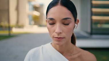 Şehir binası yakınlarında dışarıda poz veren kulaklıklı çekici bir kadının portresi. Kulaklıklı kendine güvenen iş kadını sokakta müzik dinliyor. Zarif, göz kamaştırıcı kadın kameraya özgüvenli bir şekilde bakıyor..