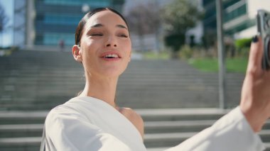 Sunny Caddesi 'ndeki modern akıllı telefonu kullanan pozitif kadın nüfuzlu biri. Açık havada video blogu kaydeden esmer bir kadın telefonda konuşuyor. Çevrimiçi iletişim kuran muhteşem bir kız..