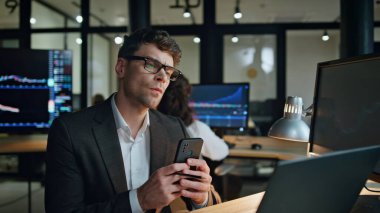 Finans müdürü ofiste bilgisayarın aşırı çalışmasına bakıyor. Odaklanmış hisse senedi tüccarları, yatırım fonu istatistiklerini analiz eder. Çevrimiçi verileri inceleyen düşünceli profesyonel cep telefonu..