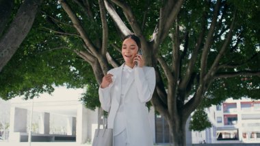 Şık iş kadını telefonu arıyor, geniş park ağaçlarının altında yürüyor, modaya uygun beyaz bir takım elbise giyiyor. Açık havada telefonla konuşan kendinden emin, başarılı bir kadın. Güzel kız arkadaşça bir cep telefonu konuşması yaptı.. 