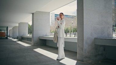 Hoparlörden konuşan başarılı bir kız zarif beyaz takım elbiseyle modern bina otoparkında dikiliyor. Modern akıllı telefondan kendine güvenen şık bir kadın sesli mesaj kaydediyor. Modayı takip eden bayan telefonda konuşuyor..