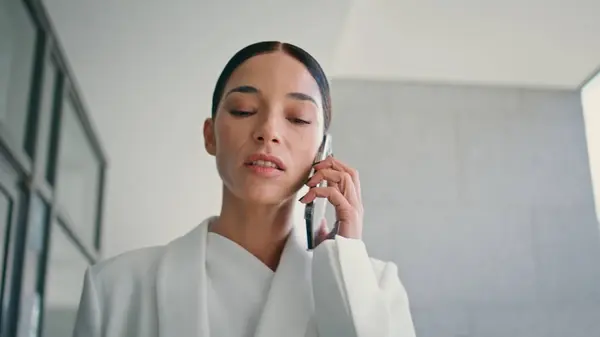 Serious lady director talking smartphone hurrying in office close up. Rich businesswoman calling discussing business problems walking in white suit. Gorgeous woman having annoying phone conversation.