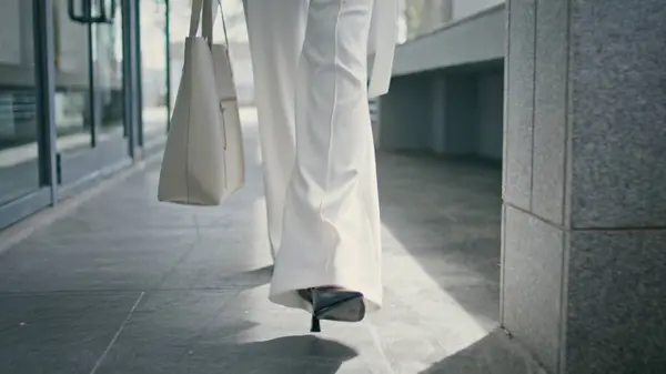 Stylish woman legs walking office in high heels close up. Unrecognizable businesswoman wearing elegant formal white suit going on work with bag. Beautiful girl feet stepping on business centre floor.