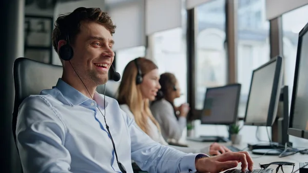 Smiling telemarketing agent talking in office. Friendly professional team help consulting clients on call. Confident joyful man woman work typing computer in data center. Helpful colleagues in headset