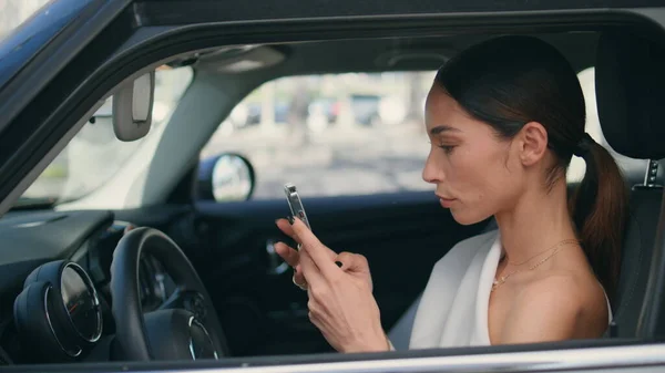 Woman driver looking telephone screen sitting car wheel closeup. Confident rich businesswoman scrolling smartphone searching information in internet. Gorgeous chic lady with phone in luxurious vehicle