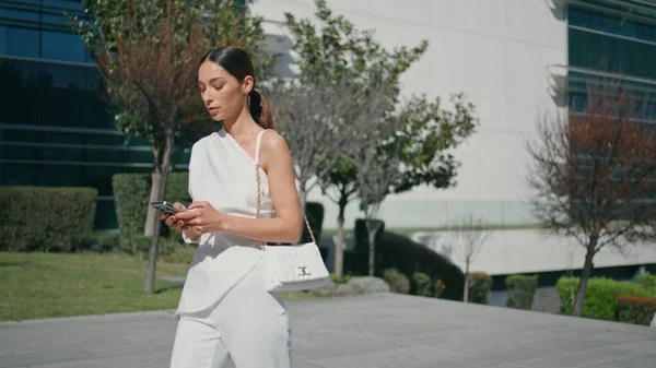 Beautiful ceo texting with work tasks on smartphone walking sunny street closeup. Chic elegant businesswoman messaging looking on telephone going to office. Rich girl business manager focused on phone