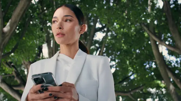 Beautiful lady looking smartphone walking city garden alone close up. Successful woman conducting business correspondence using modern telephone outdoors. Confident businesswoman scrolling phone on go