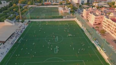 Yaz akşamı hava manzaralı güzel bir köy futbol stadyumu. Çeşitli dinlenen insanlarla yeşil çimen futbol sahası. Yumuşak güneş ışığı altında pitoresk şehir manzarası. Spor oyunu için şehir altyapısı.