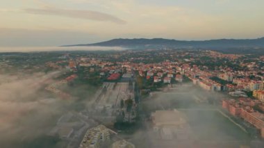 Akdeniz 'in sakin gökyüzü altında bir panorama kasabası. Yazın alacakaranlıkta okyanus kıyısına kurulmuş insansız hava aracı manzaralı muhteşem bir şehir. Kentsel fayanslı çatı binalarını kaplayan hafif sis. Panoramik şehir manzarası.