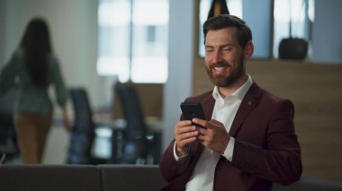 Modern ofis içinde cep telefonu kullanan gülümseyen bir profesyonel. Mutlu başarılı iş adamı cep telefonu ekranına bakıyor. Finans müdürü şirket planını okuyor. Neşeli işçi konsepti.