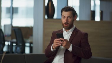Başarılı bir iş adamı, gülümseyen akıllı telefon görünümlü, büyük, rahat bir şirket salonu. Modern ofiste cep telefonuyla 