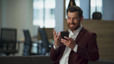 Kızgın yönetici, modern ofis iç çekimlerinde mesaj yazıyor. Ciddi bir iş adamı, şirket konforlu salonundaki akıllı telefon ekranına dokunuyor. İdari profesyonel girişimci çalışma konsepti.