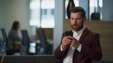 Modern büyük ofis içinde ciddi bir iş adamı cep telefonuyla sohbet ediyor. Odaklanmış girişimci akıllı telefon şirket binasına mesaj yazıyor. Profesyonel finansal yönetici başarılı çalışma konsepti.