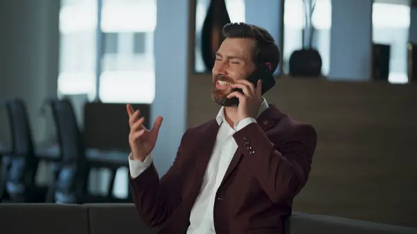 Cheerful manager making call in office sofa closeup. Smiling joyful business manager discussing financial marketing plans. Beard man talking mobile phone in modern hall. Ceo corporate work concept.