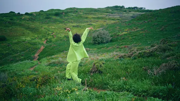 Stylish african american woman performer dancing walking on green field path cloudy evening. Professional girl dancer performing sensual modern dance on gloomy meadow. Curly lady moving body outdoors.