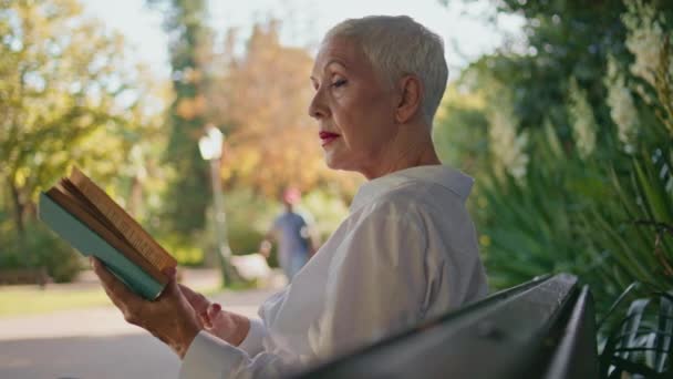 退休妇女翻阅绿地公园里的书 专注的白发女士一个人在平静的周末享受着小说 时尚的资深坐在长椅上保存着文学作品 退休休闲 — 图库视频影像