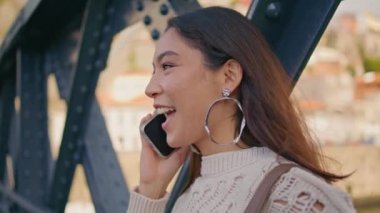 Neşeli esmer, hücreden bahseden Demir Köprü 'de iyi haberleri paylaşıyor. Hafta sonu yürüyüşü için akıllı telefondan arayan mutlu Meksikalı kadın. Gülümseyen siyah saç modeli telefonla konuşuyor. Nöbetçi heyecanlı kadın