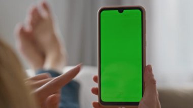 Kadın parmağı yeşil ekran akıllı telefona dokunuyor, kanepeyi kapatıyor. Kimliği belirsiz bir kadın evde uzaktan çalışan kroma anahtarı yazıyor. Elinde model cep telefonu olan tanınmamış bir kız internete takılıyor.