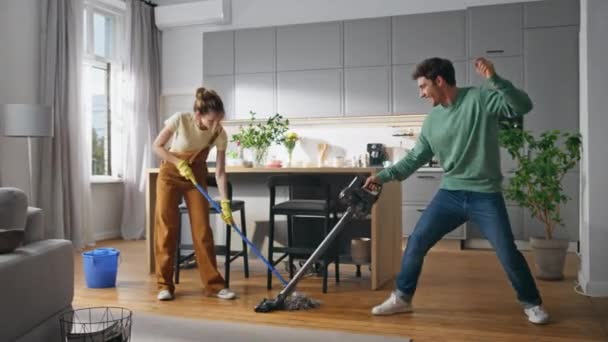 有趣的夫妇一起打扫房子 安静的女人在明亮舒适的房间里用吸尘器清洁地板的快乐男人 年轻的配偶在家里开玩笑 家庭工作生活方式概念 — 图库视频影像