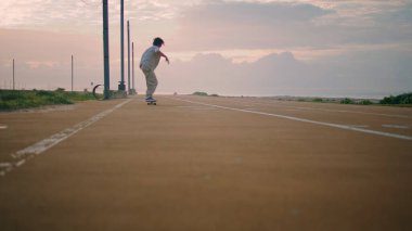 Günbatımı okyanus arka planında havalı bir hippi atlama tahtası. Aktif kaykaycı çocuk yaz seti sürüşünün tadını çıkarıyor. Genç sporcu kaykayı dengede tutuyor. Akşam koşu bandında numara yapıyor. 