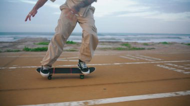 Deniz kıyısında kaykay süren tanınmayacak kadar enerjik bir adam. Genç kaykaycı ayakları uzun tahta üzerinde zıplıyor ve ağır çekimde numara yapıyor. Modern genç okyanusta kaykay yapıyor. Sıra dışı spor.