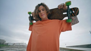 Portre patencisi çocuk yaz parkında kameraya poz veriyor. Modern kaykayı omuzlarında tutan neşeli adam gülümsüyor. Piercingli neşeli çekici adam. Dışarıda rahatla.