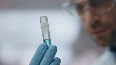 Yakın plan yetenekli bilim adamı gelişmiş laboratuarda tıbbi hazırlık yapan bir test tüpüne bakıyor. Güvenlik gözlüklü genç araştırmacı uyuşturucuları kontrol ediyor. Ciddi bir doktor mikrobiyoloji araştırması düşünüyor..