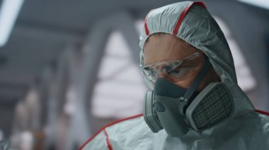 Profesyonel kimyager laboratuarda koruyucu üniforma giyen bir sıvıyla matarayı inceliyor. Kimyasal deney yapan dezenfekte üniforması giyen ciddi bir adam. Koronavirüs salgını.