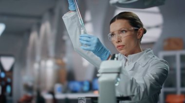 Bilim adamı aşı araştırması yapıyor. Test tüpünü yakından inceliyor. Mikro pipetle ilaç analiz ederek numunelerle çalışan gülümseyen kadın araştırmacı. Gelişmiş bilim laboratuvarında deneyler yapan kimyager.