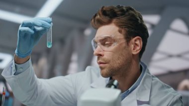 Doktor modern laboratuarda çalışan ilaç örneklerini araştırıyor. Güvenlik gözlüklü araştırmacı ilaçlı test tüpüne bakıyor. Yeni aşıyı inceleyen deneyimli laboratuvar bilim adamı..