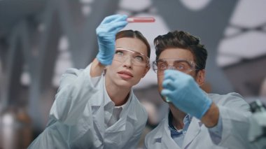 Biyoteknoloji laboratuarında aşı örneklerini inceleyen iki araştırmacı. Profesyonel bilim adamları test tüpündeki ilaçlara bakıyor. Kadın kimyager, erkek teknisyene deneysel ilaçlar gösteriyor..