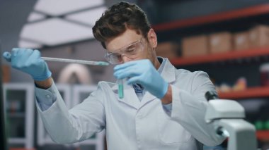 Gelişmiş klinikte yenilikçi ilaçlarla ilgili deneyler yapan profesyonel bir doktor. Ciddi bir bilim adamı deney tüpünü pipetle dolduruyor. Gözlüklü araştırmacı aşıyı araştırıyor..