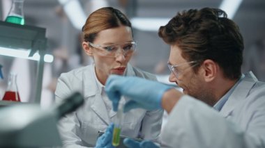 Gülümseyen klinik çalışanları biyoteknoloji laboratuvarında tıbbi araştırma geliştiriyorlar. Gülümseyen kadın bilim adamı test tüpü tutan adamla tedaviyi tartışıyor. Aşı örneklerinde çalışan mutlu doktorlar..